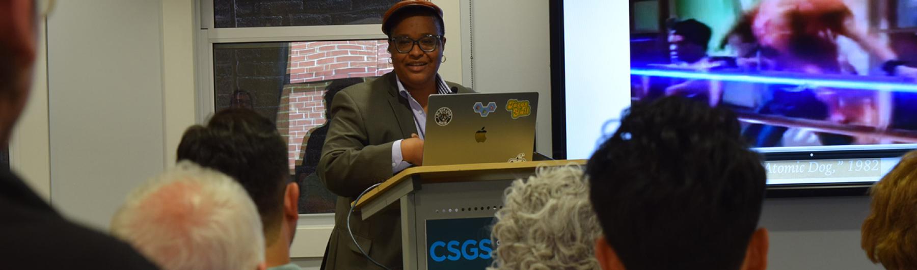 People seated listening to a speaker and looking at a presentation.